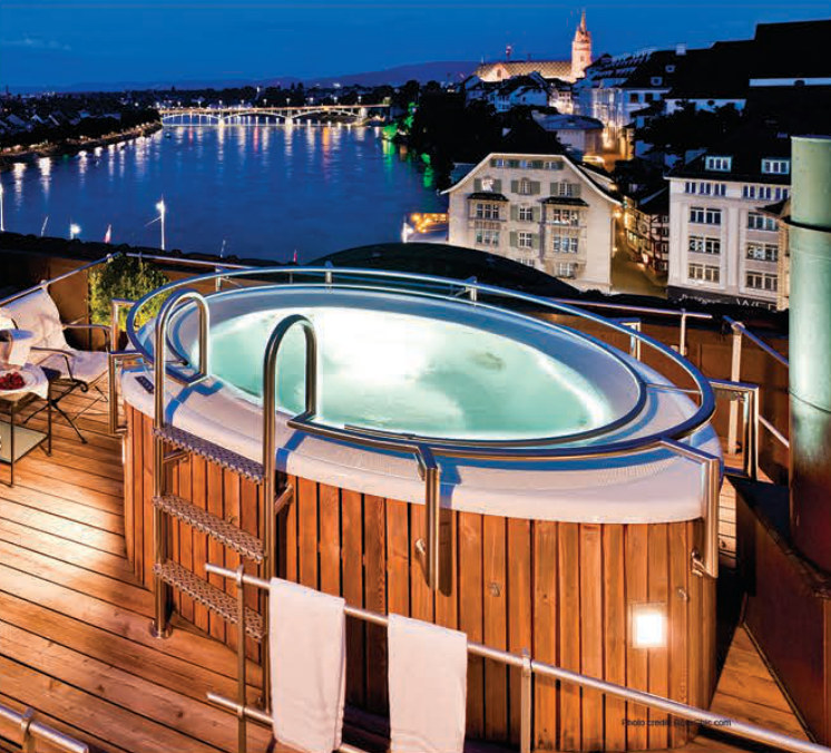 A wood-clad hot tub on a rooftop terrace overlooking a river at dusk